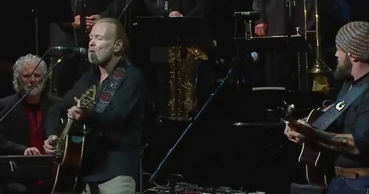 A man with a beard plays guitar and sings on stage with a band.