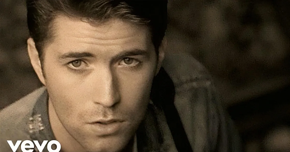 A man with short hair and a serious expression, wearing a dark jacket, is the main subject.