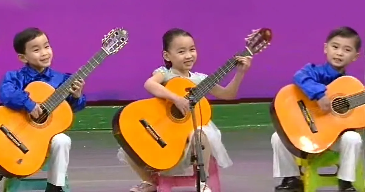 Three children play guitars on stage, smiling and enjoying their performance.