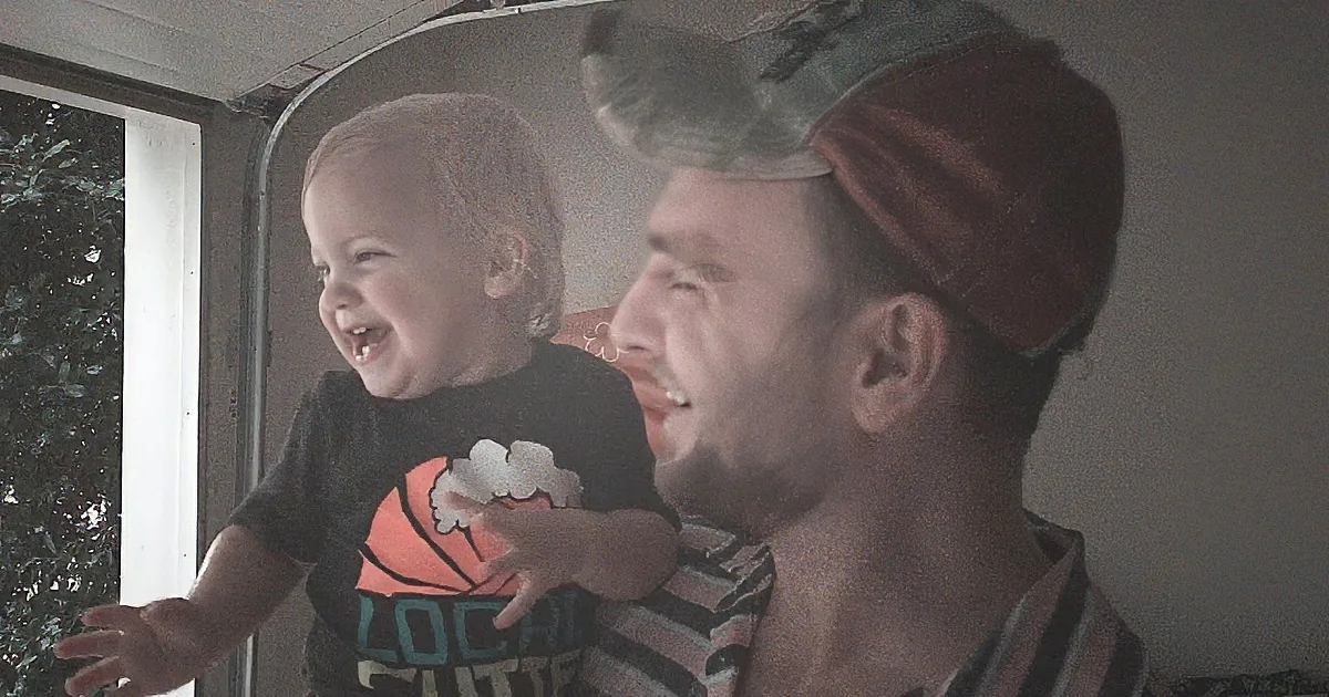 A man holds a laughing baby, both wearing striped shirts, in a dimly lit room.
