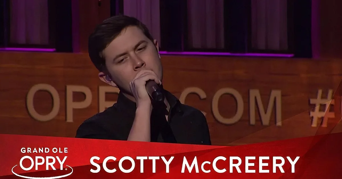 Scotty McCreery sings passionately at the Grand Ole Opry, holding a microphone.