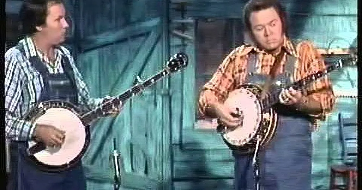 Two men play banjos in a rustic setting, one wearing overalls, the other in a plaid shirt.