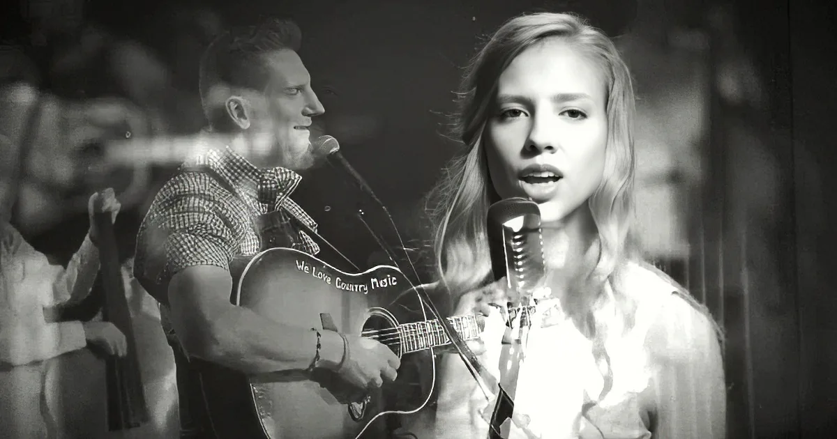 A woman sings into a microphone, accompanied by a man playing guitar and another musician in the background.