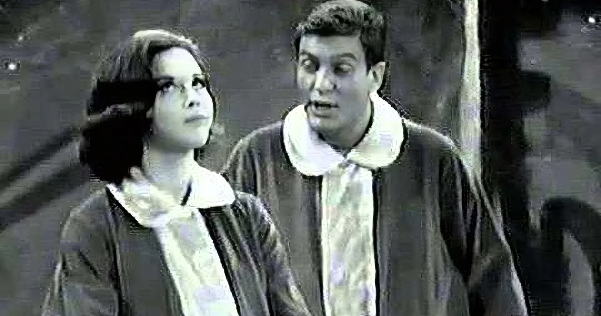 A man and woman in formal attire stand together, the woman looking up, the man looking ahead.