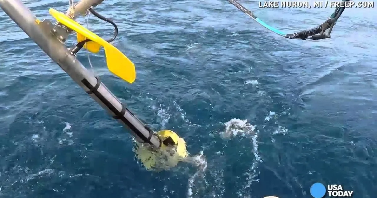 A yellow underwater vehicle is being lowered into Lake Huron by a boat.