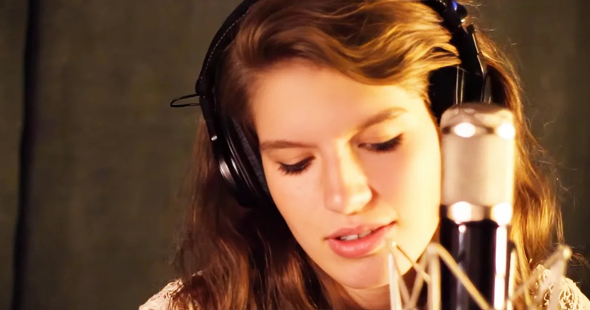 A person wearing headphones is singing into a microphone in a recording studio.
