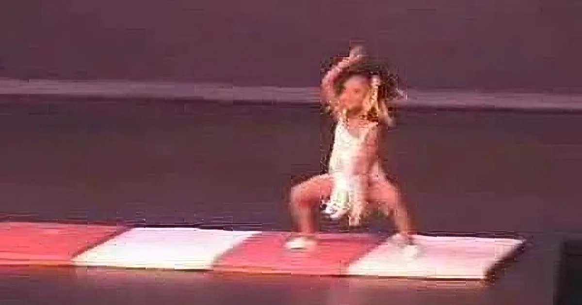 A person in a white outfit is performing a dance move on a stage with red and white blocks.