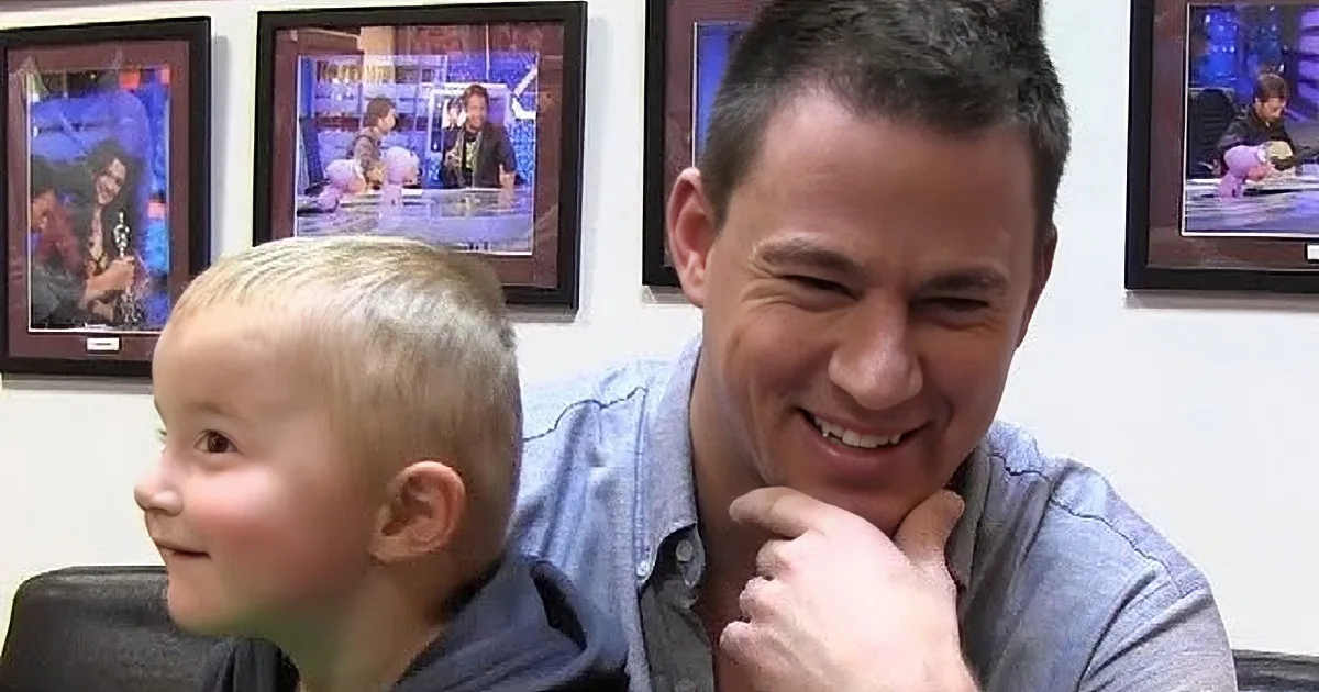 A man and a young boy are smiling in a room with framed pictures on the wall.