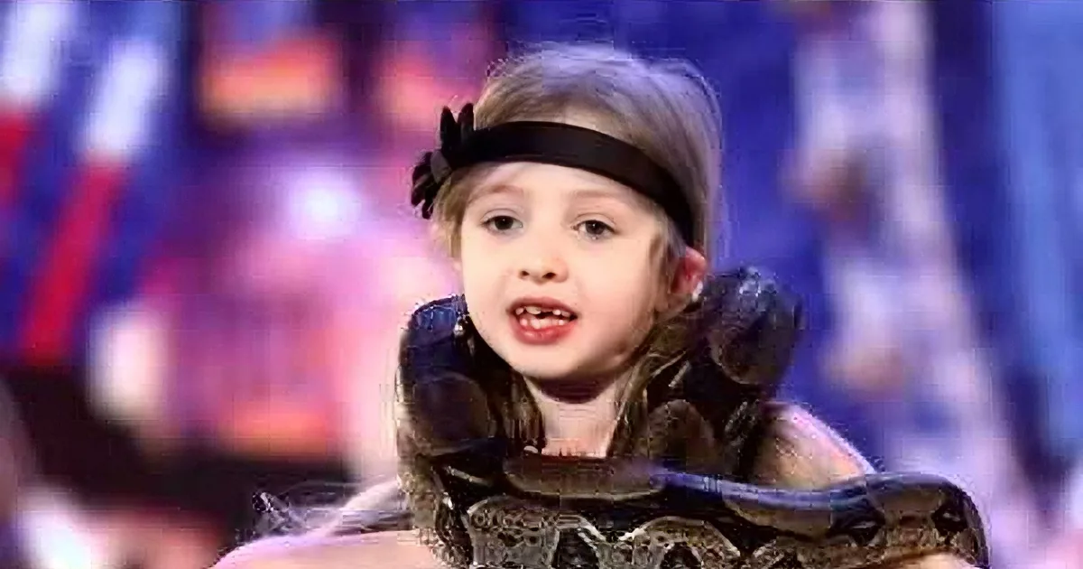 A young girl with a snake draped around her neck, wearing a black headband, in a colorful background.