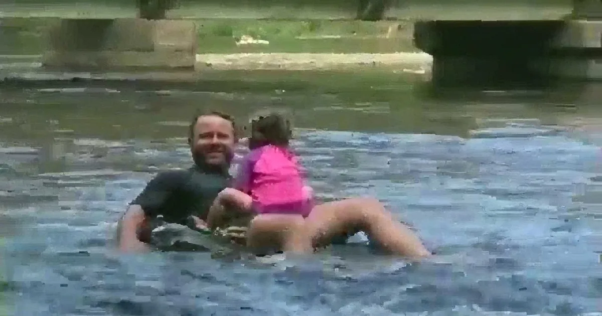 A man and two children, dressed in pink, are floating in a river, appearing to enjoy the water.