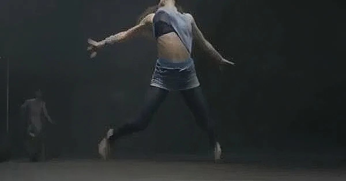 A dancer in mid-air, wearing a blue top and black pants, with another person in the background.