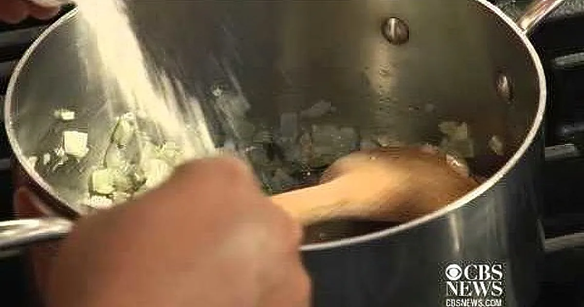 A hand stirs a pot of food with a wooden spoon, showing a close-up of the cooking process.