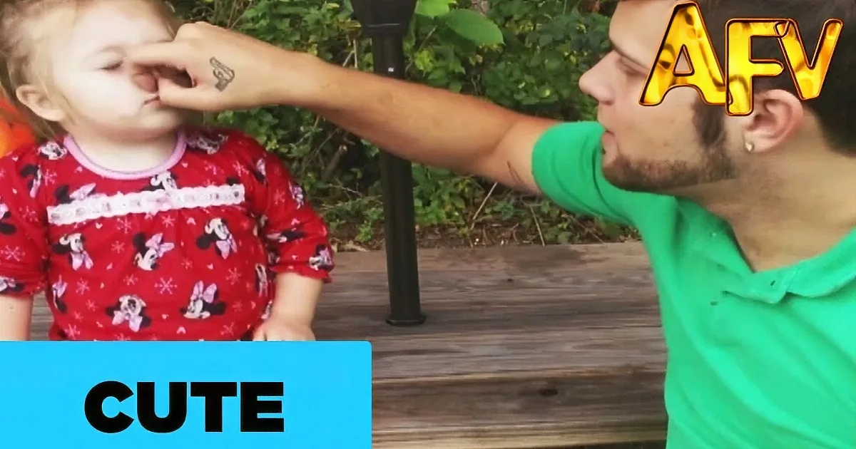 A man in a green shirt playfully touches a child's nose at a wooden picnic table.