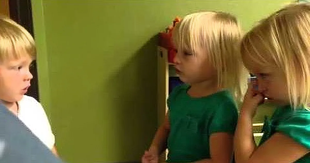 A young child in a green shirt is looking at another child who is sitting and appears to be talking.