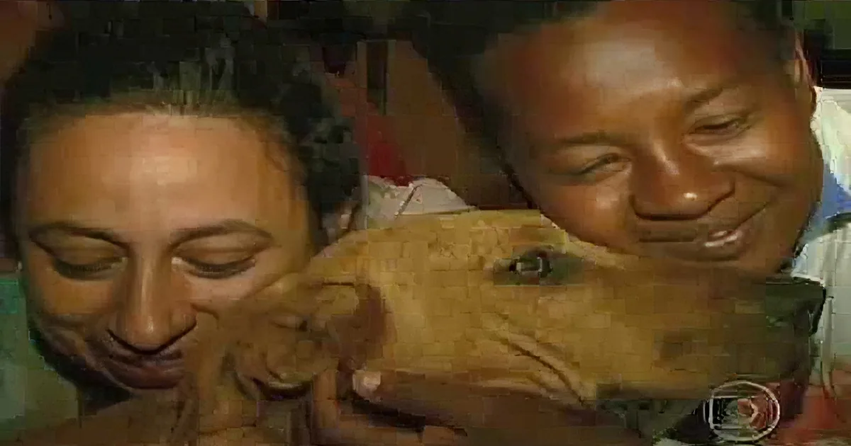 A man and woman are smiling while holding a small brown puppy.