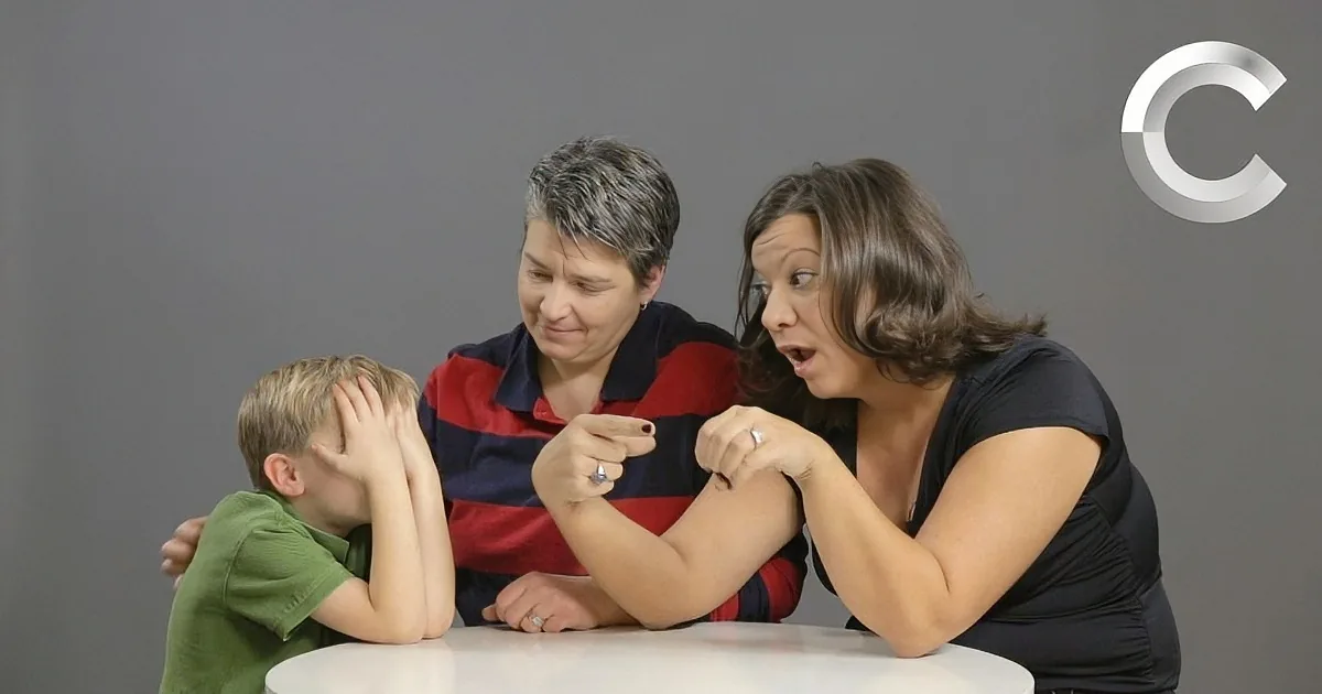A woman in a black shirt points while another woman in a red and blue striped shirt leans over a table with a child in a...