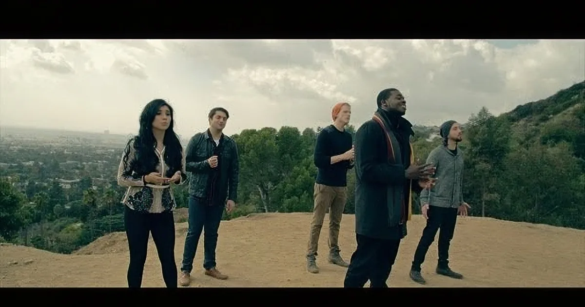 A group of five people stands on a hill overlooking a cityscape under a cloudy sky.