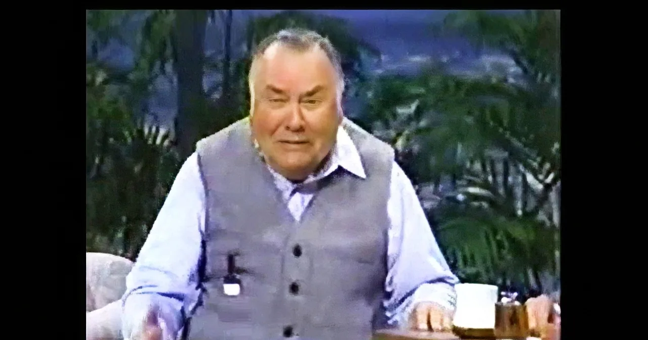 An older man in a vest and shirt sits at a table with a mug, appearing to speak or react.