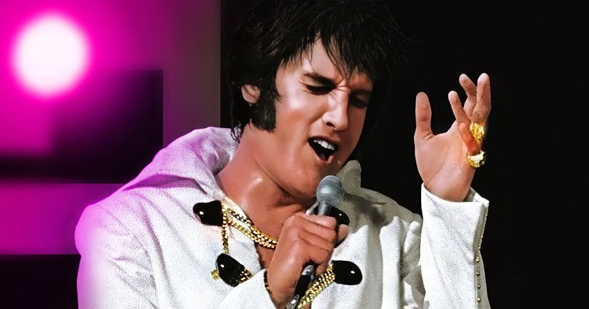 Elvis Presley in a white suit with gold accents, singing into a microphone with a dynamic pose.