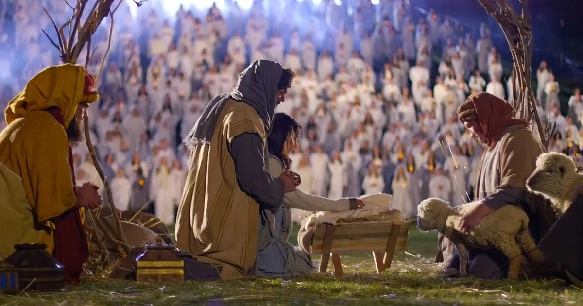 A group of people in robes kneel in front of a large crowd, with one person holding a lamb.