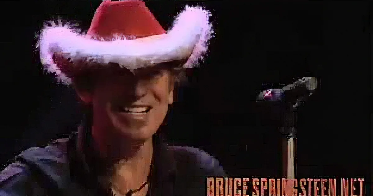 A person wearing a Santa hat and a black shirt is smiling, with a microphone and dark background.