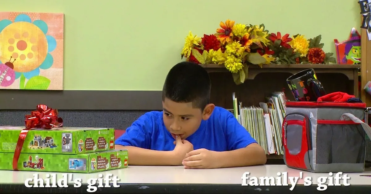 A boy sits at a table with two gift boxes labeled "child's gift" and "family's gift," surrounded by colorful decorations.