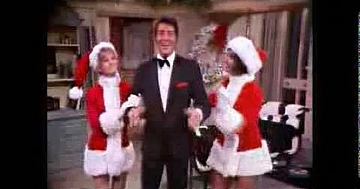 A man in a tuxedo dances with two women in Santa outfits in a festive setting.