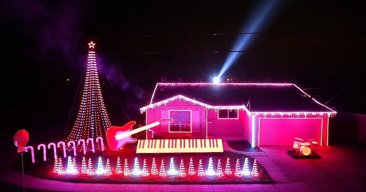 A house adorned with vibrant pink and white lights, featuring a Christmas tree, musical instruments, and a spotlight.