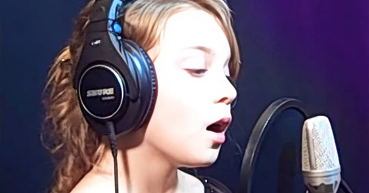 A person wearing headphones sings into a microphone in a recording studio.