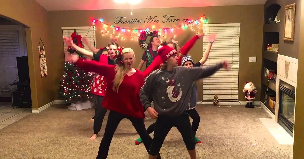 A group of people in festive attire dances joyfully in a living room decorated for Christmas.