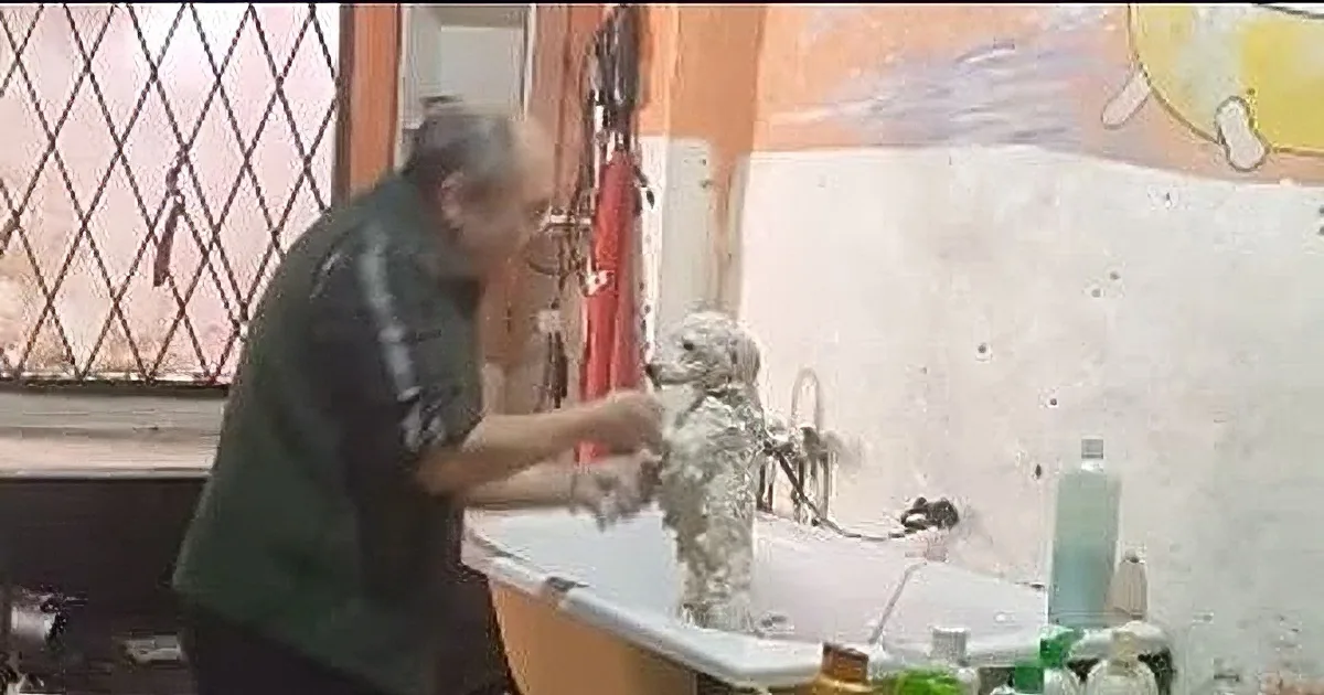 A man in a green jacket is working on a sculpture in a workshop with various tools and materials around him.