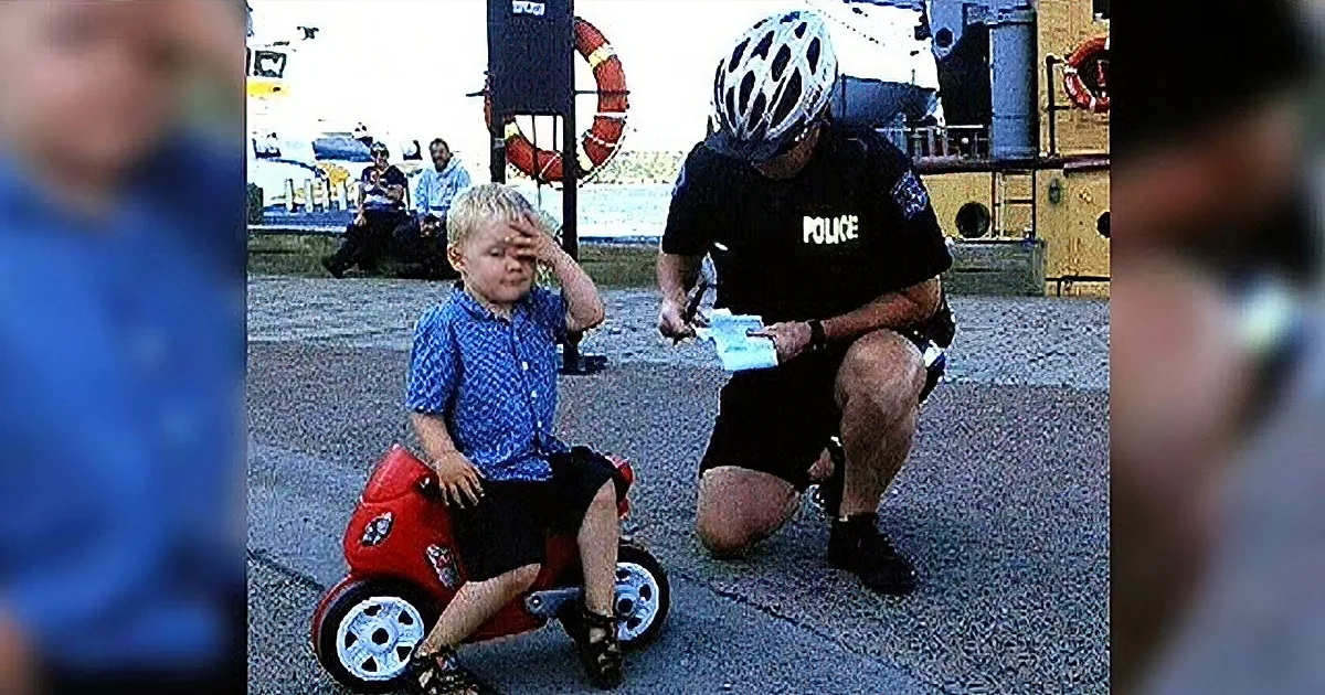 A police officer assists a child on a small motorcycle at a public event.