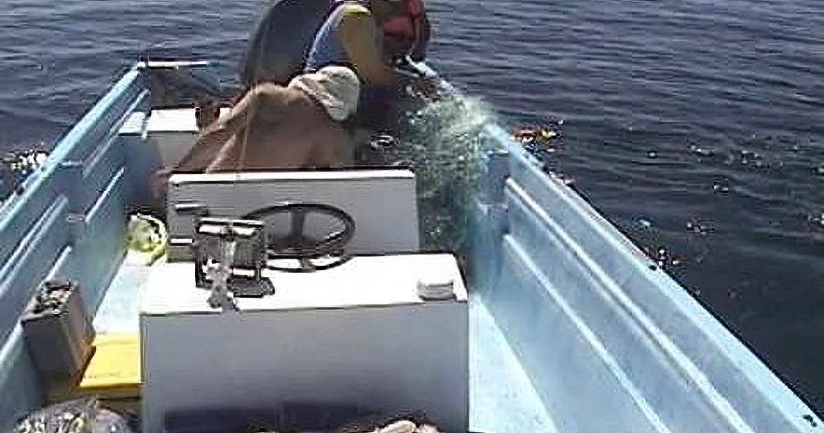 A person in a small boat is fishing, with water splashing around and debris on the boat.