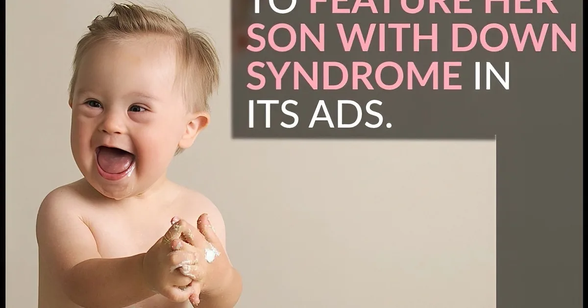 A joyful toddler with Down syndrome smiles widely, hands covered in white substance, against a neutral background.