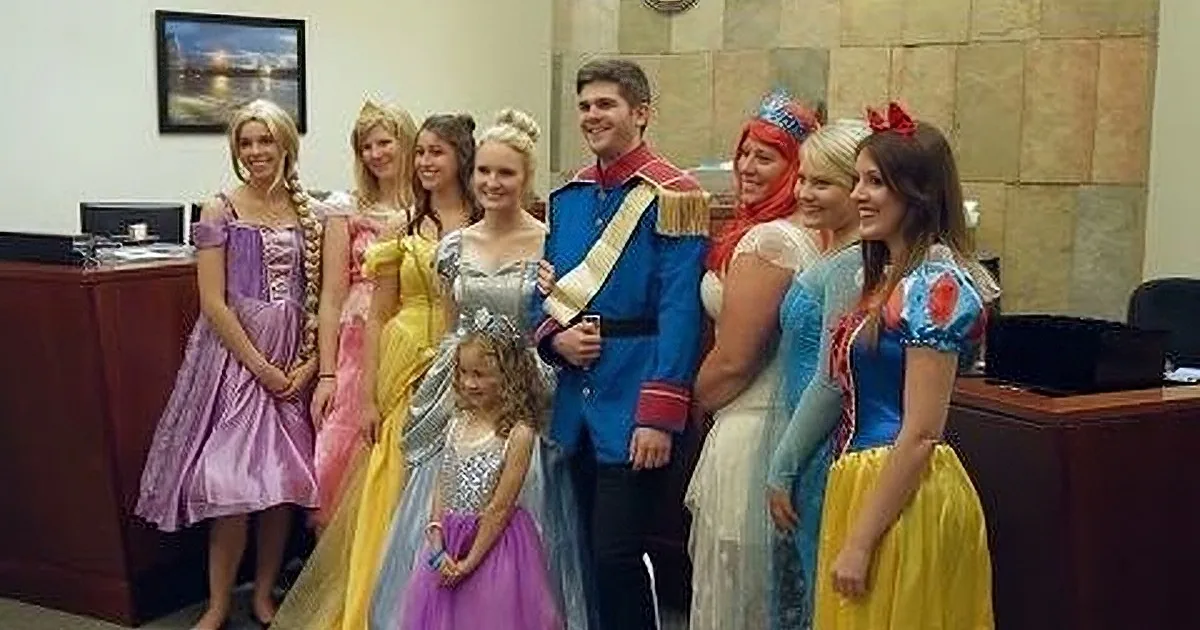 A group of people dressed as Disney princesses and a prince pose for a photo in an office setting.