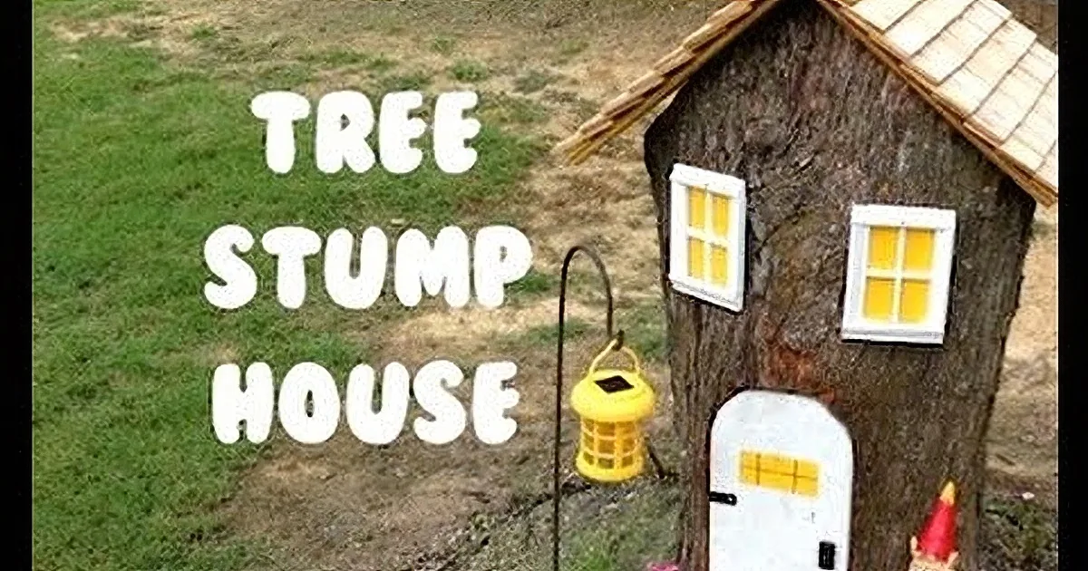 A whimsical tree stump house with small windows, a thatched roof, and a bird feeder hanging nearby.