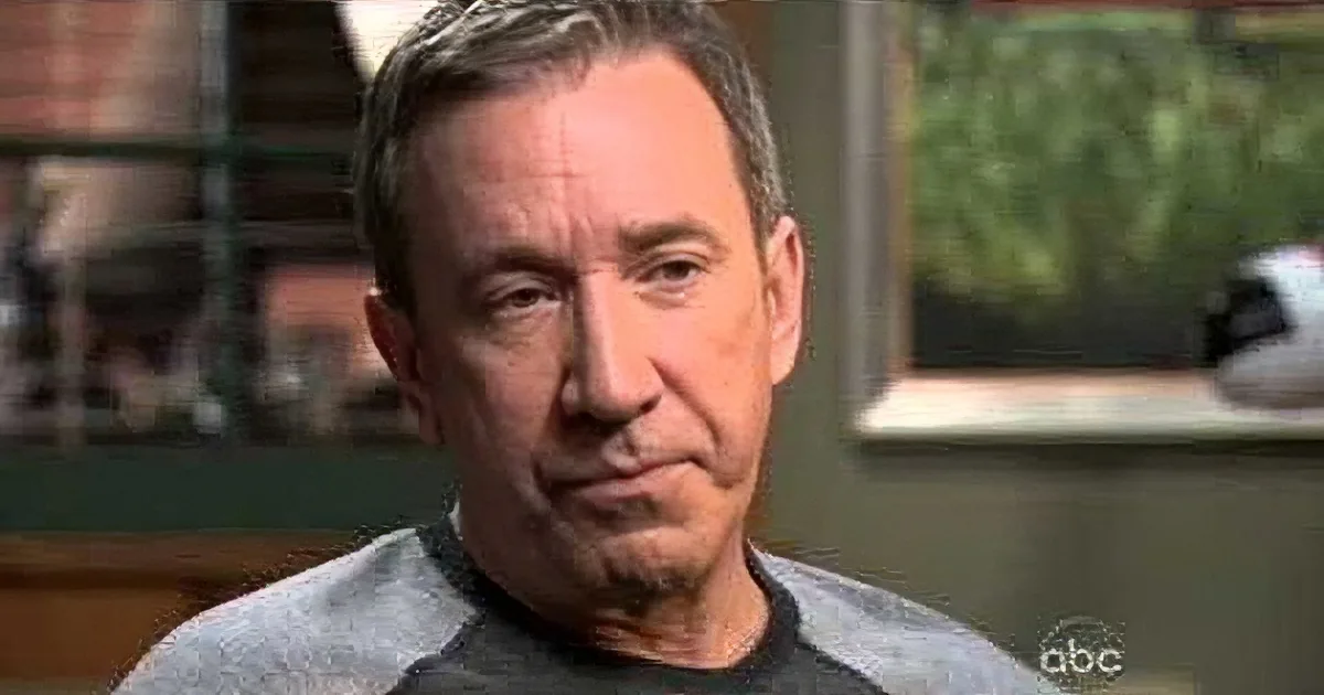 A man with short gray hair, wearing a gray and black shirt, is speaking in an interview setting.
