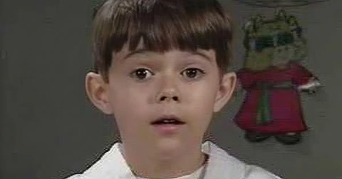 A young boy with short brown hair and a surprised expression, wearing a white shirt.