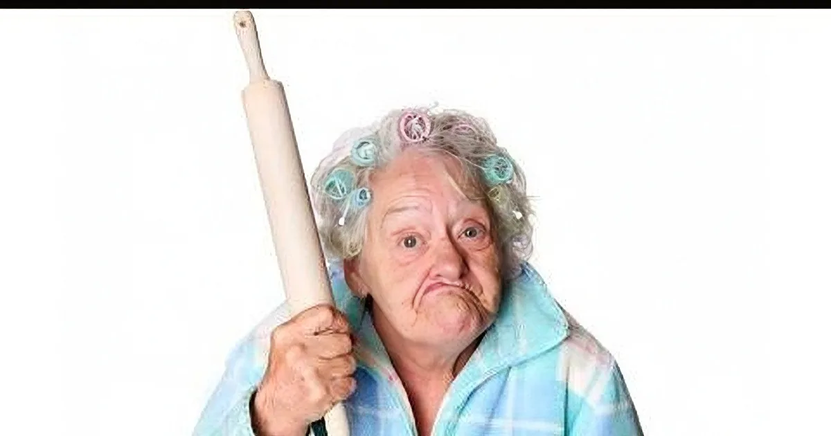 An elderly woman with curlers in her hair holds a rolling pin, wearing a blue and white striped shirt.