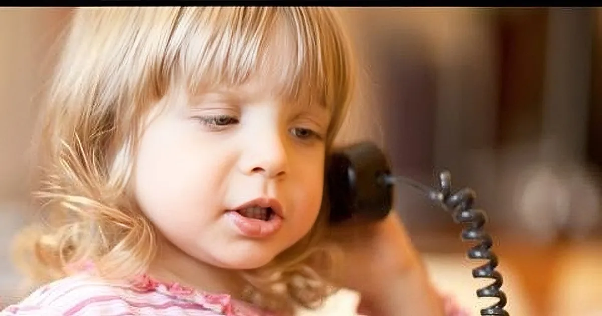 A young child with blonde hair, wearing a pink striped shirt, appears to be speaking or singing.