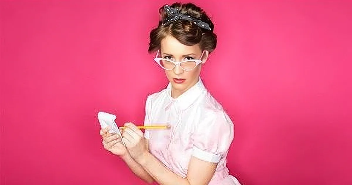 A woman in a pink dress and glasses holds a pencil and paper against a vibrant pink background.