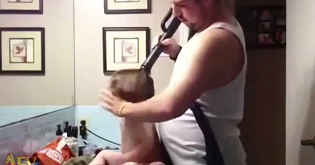 A man in a white tank top holds a microphone, singing while a child sits on his lap.