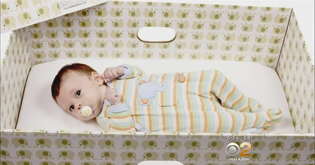 A baby in striped pajamas lies in a crib with elephant-patterned bedding.