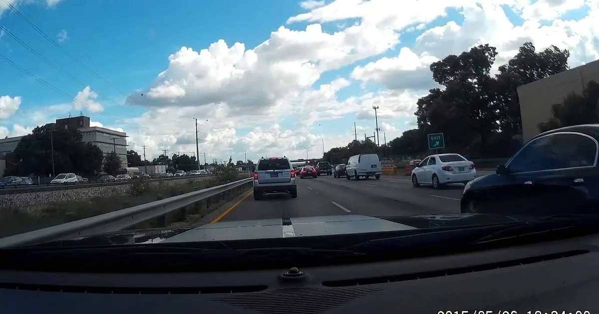 A car's dashboard view shows a traffic jam on a highway under a partly cloudy sky.