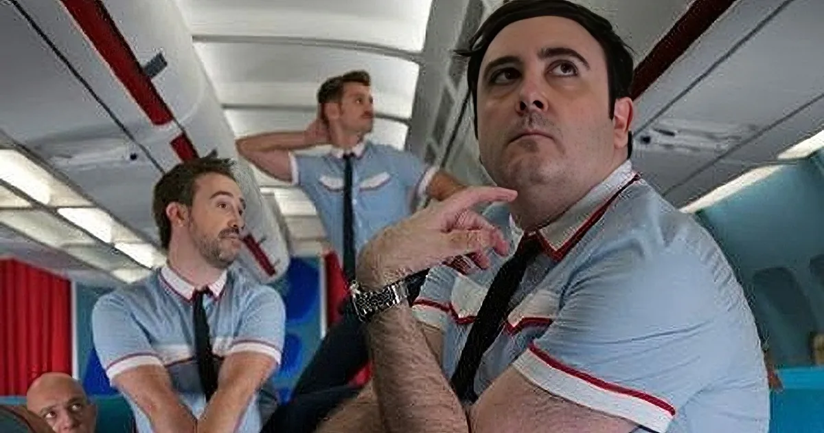 A man in a striped shirt and tie is pointing upwards, looking up at something in the airplane cabin.