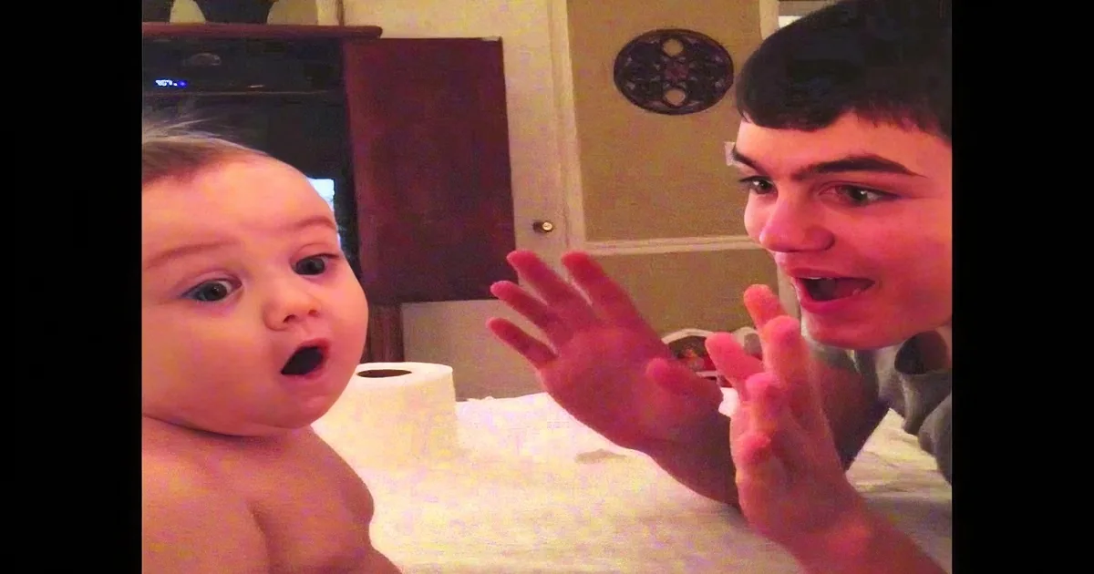 A baby and a young person are interacting with toilet paper rolls on a table.