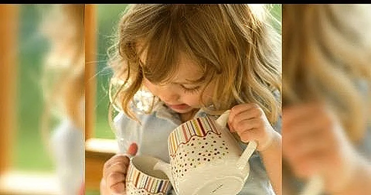 A young child with curly hair is holding a cup and looking down, seemingly focused on something in their hands.