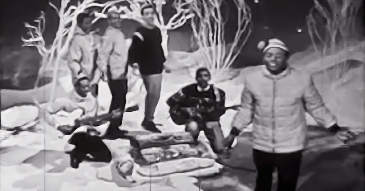 A man in a white jacket and hat dances in front of a group of people in a snowy, surreal setting.