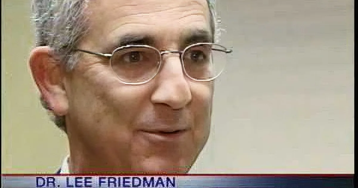 A man wearing glasses and a suit is shown on a news broadcast, identified as Dr. Lee Friedman.