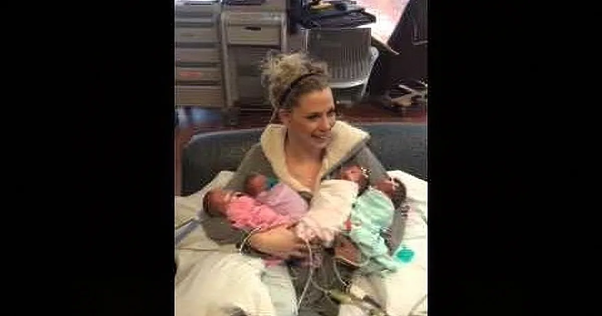 A woman holds two newborn babies wrapped in blankets, smiling in a hospital setting.